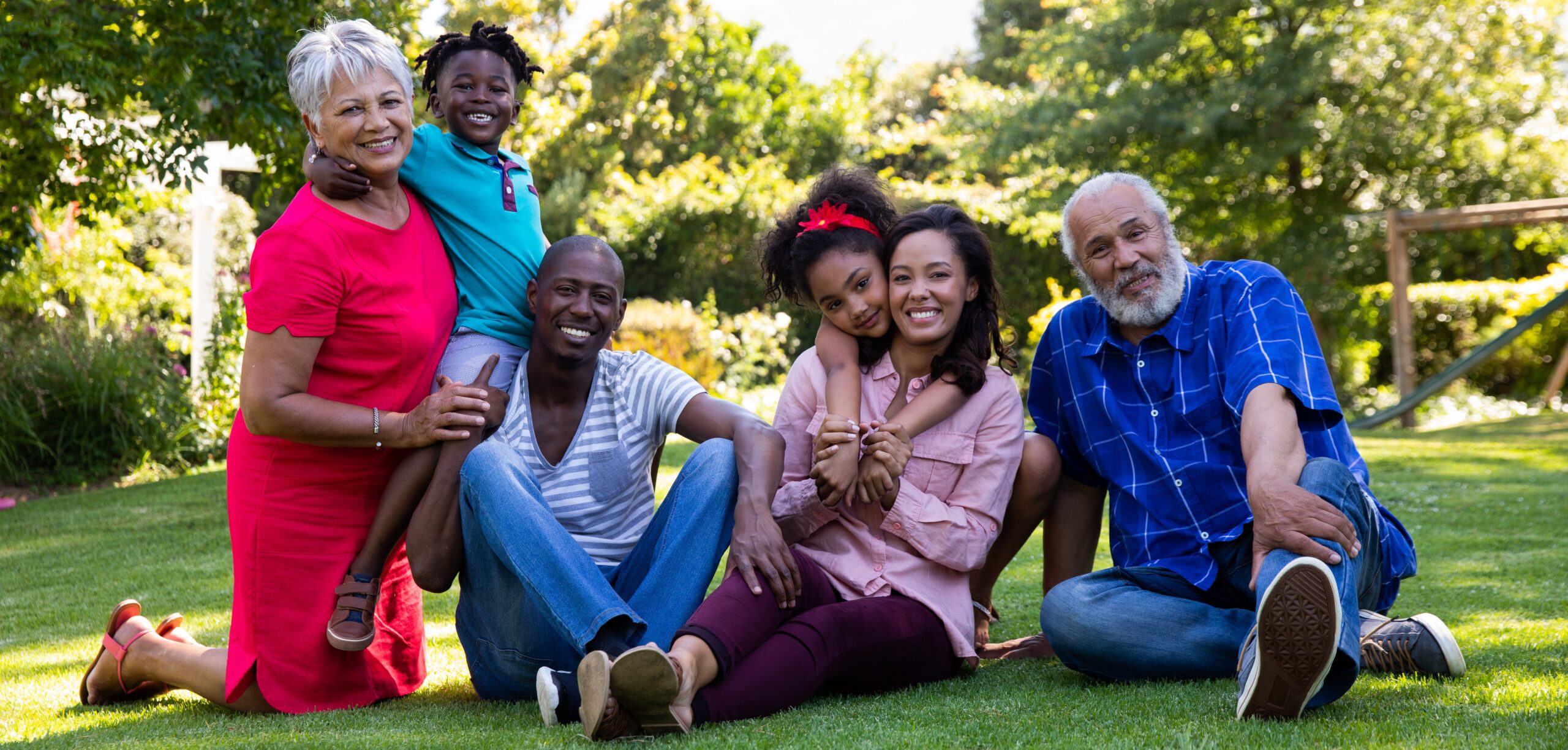 Three generations of a smiling family sit together on grass in a sunny garden, looking happy and carefree. Thanks to Prospan’s effervescent cough tablets, everyone enjoys the fresh air with ease amid the trees and vibrant greenery.