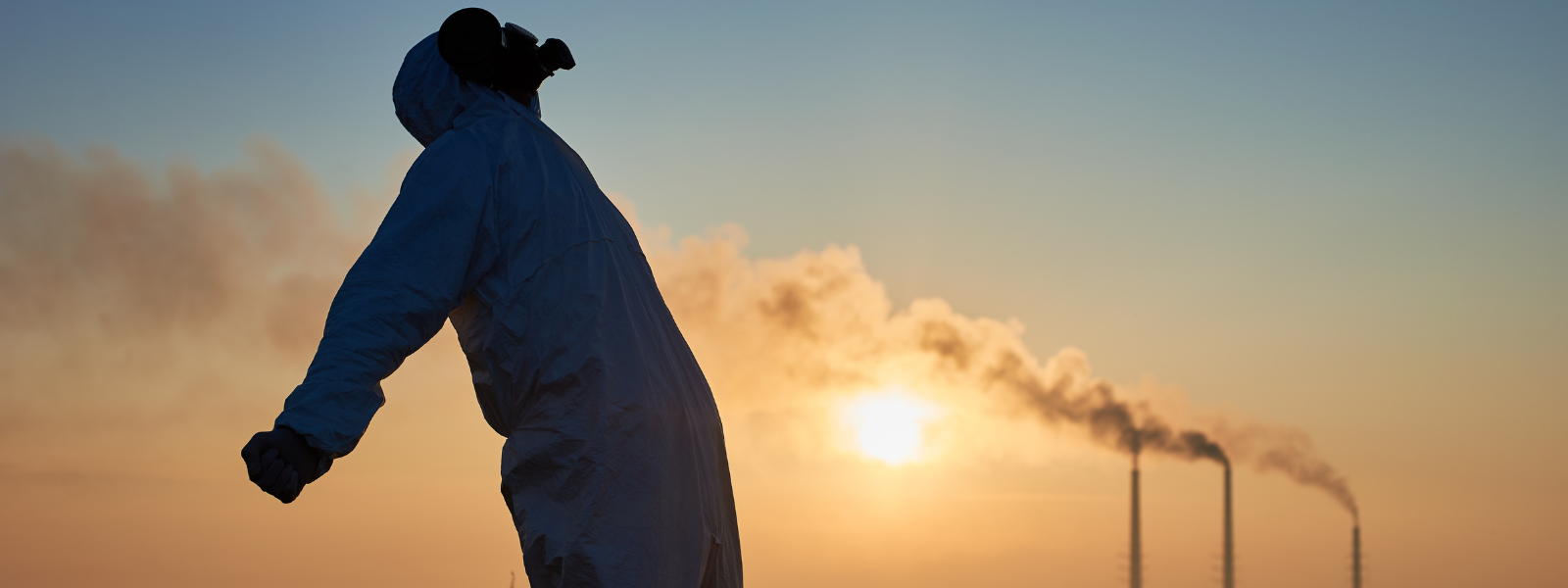 What effect does air pollution have on our health ? A person wearing a protective suit and gas mask stands outdoors at sunset, with industrial chimneys in the background emitting smoke into the sky.